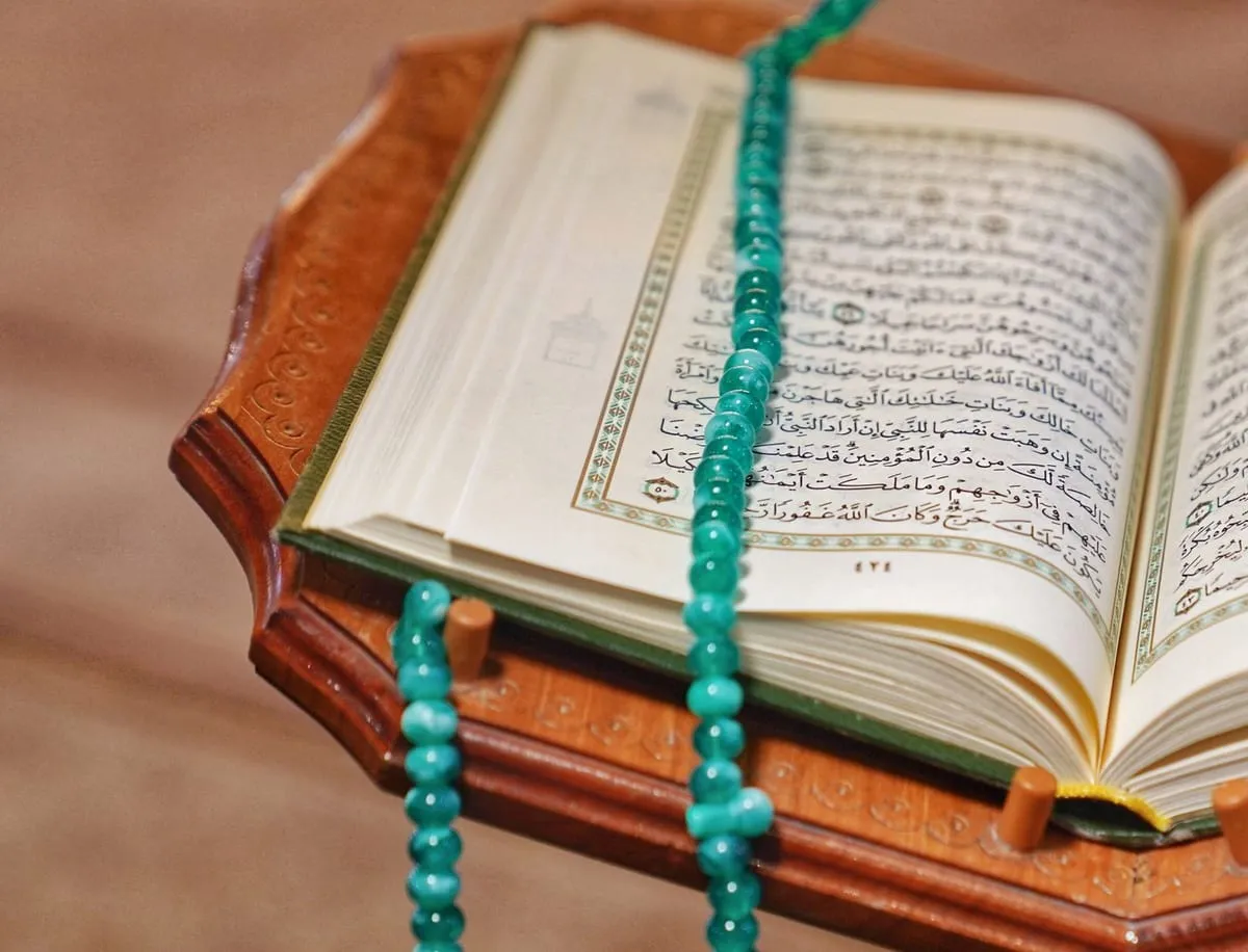 An open Quran on a carved wooden stand with prayer beads