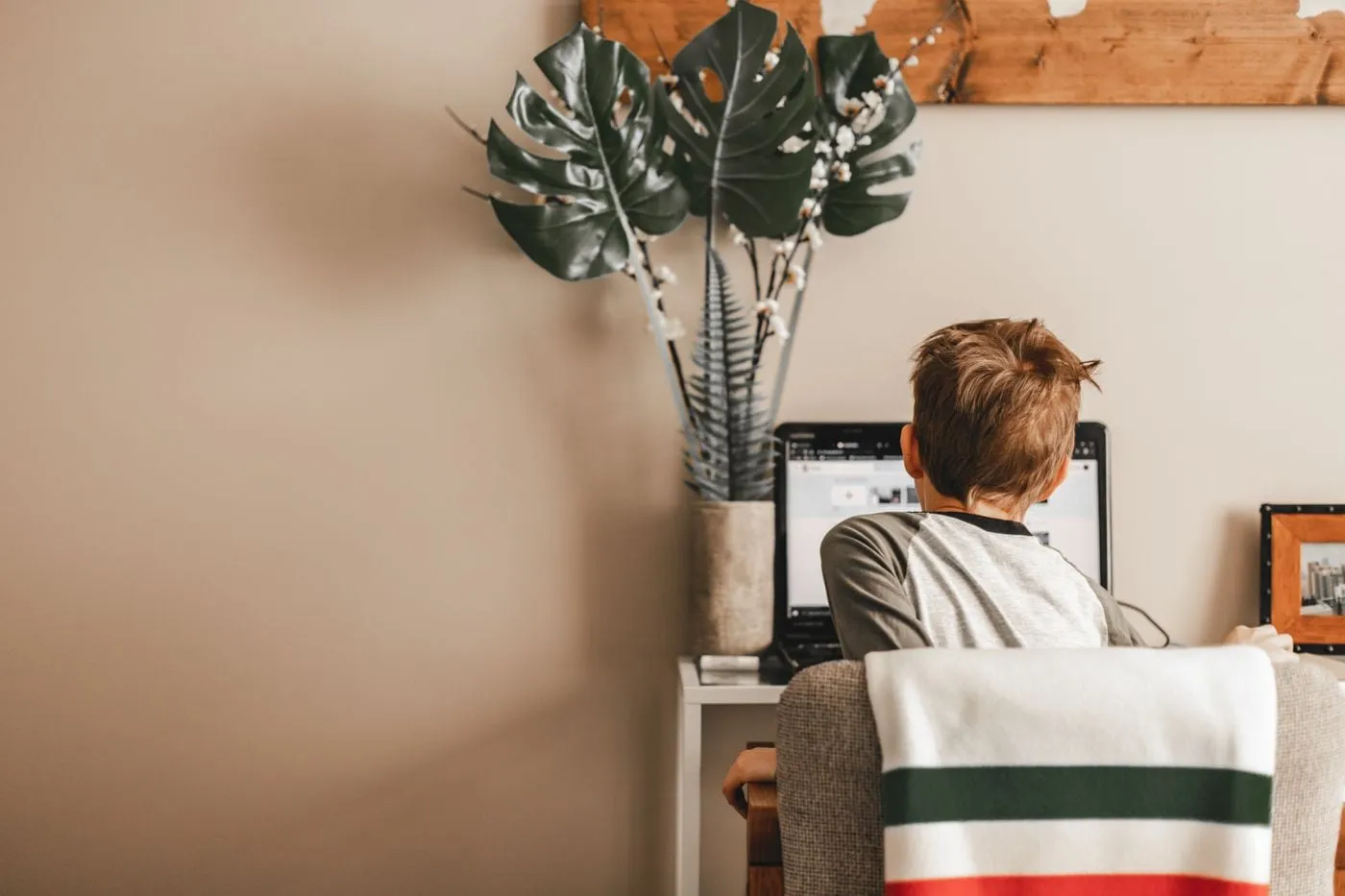 A child seen from behind, studying at a laptop in a quiet corner at home
