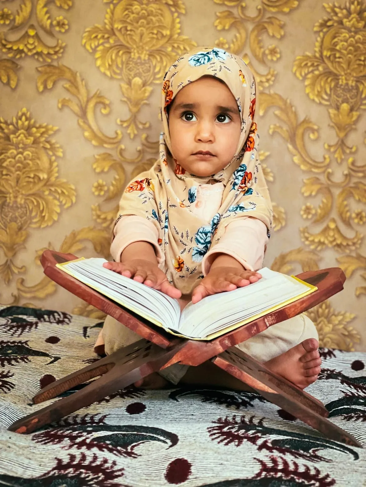 A young child with an open Quran on a wooden stand