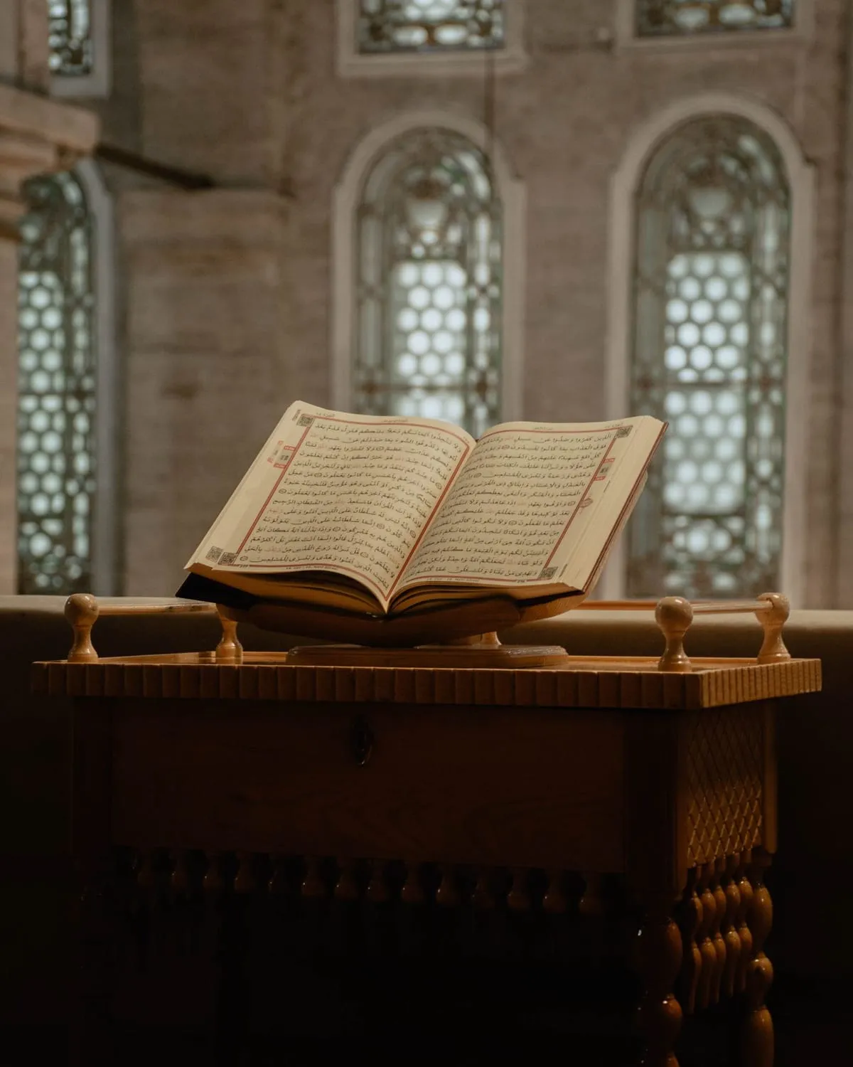 An open Quran on a wooden stand in a mosque with arched windows